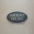 Oval metal sign with 'OUR PLACE EST. 2021' text on a beige background