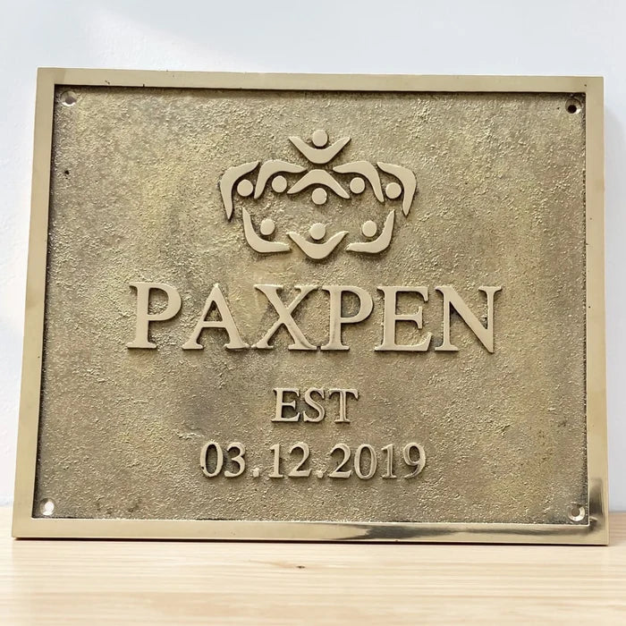 Brass plaque with 'PAXPEN' logo and establishment date on a white background