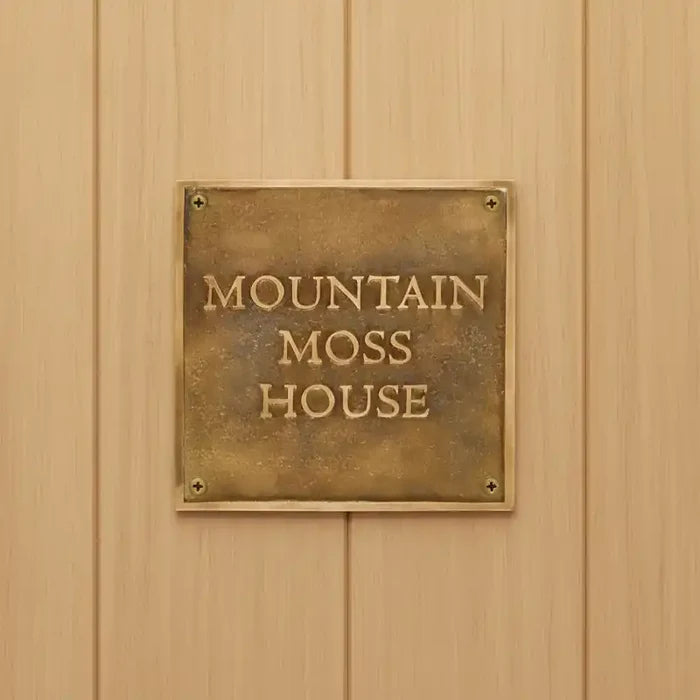 Brass plaque with 'Mountain Moss House' on a wooden wall