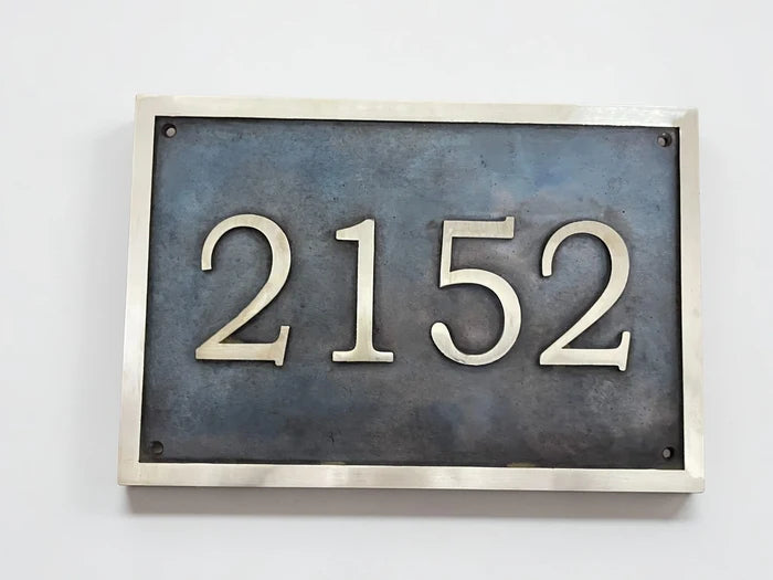 House number plate with '2152' on a metallic frame against a white background