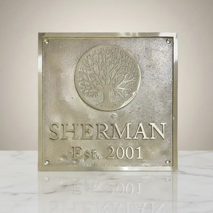Custom brass address plaque | Decorative plaque with tree design and text on a marble surface.