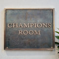 Bronze address plaque  with 'Champions Room' text on a white wall