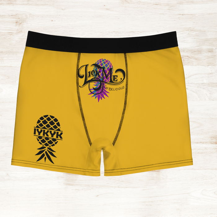 Yellow boxer briefs with black pineapple design and colorful logo on a light wooden surface