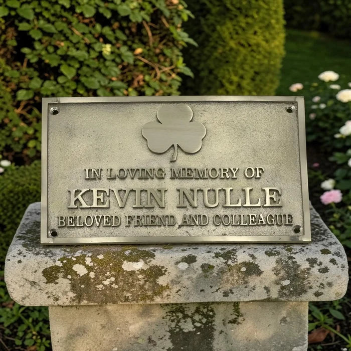 Memorial plaque with a shamrock symbol for Kevin Nulle in a garden setting.