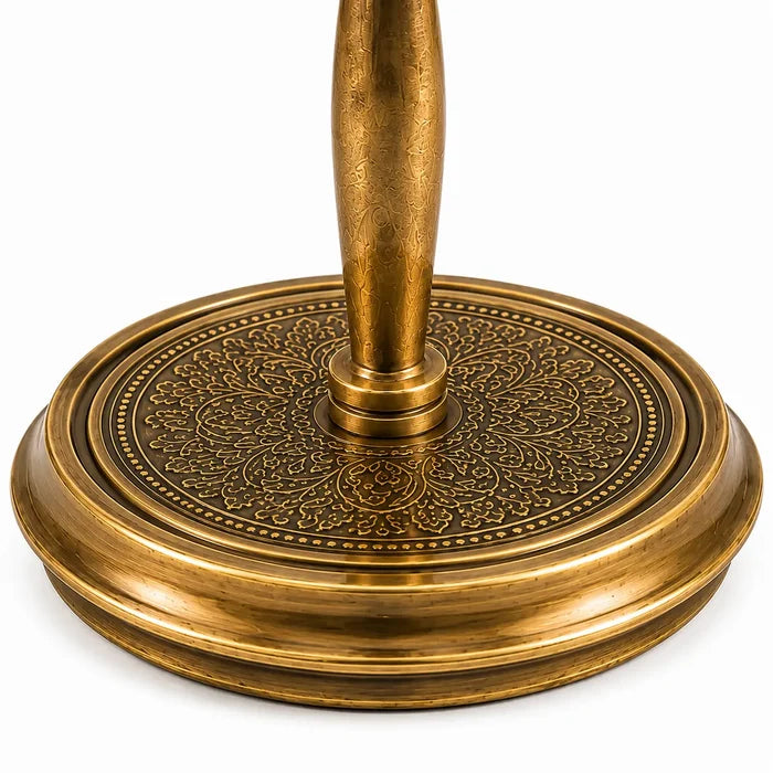 Close-up of an ornate brass table base with a circular, intricately embossed floral pattern and a central pedestal stem, shown on a white background.