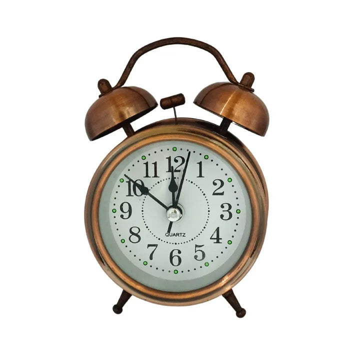A vintage-style brass alarm desk clock with a white face, black hands, and a brass stand, featuring a traditional design with a twin bell alarm.